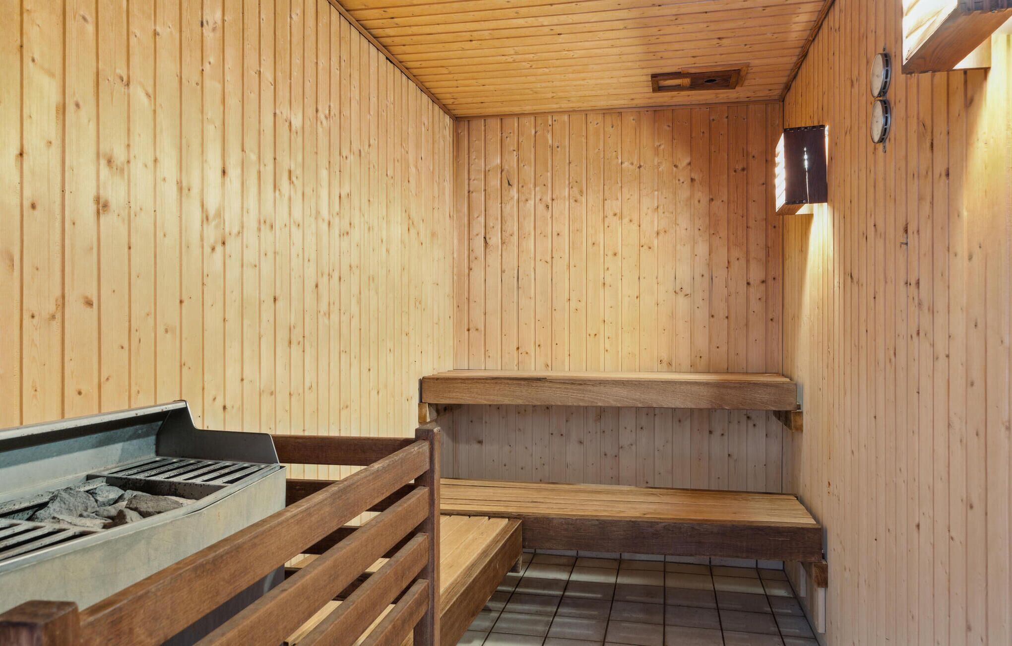 Un sauna aux murs et aux bancs en bois, doté d’un sol carrelé et d’un élément chauffant visible.