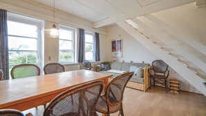 Et hyggeligt rum med et træspisebord, fletstole, en sofa og udsigt til det fri gennem store vinduer.
