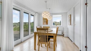Uma sala de jantar com mesa e cadeiras de madeira, janelas amplas e vista para o exterior.