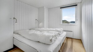 Quarto com duas camas, paredes brancas, janela com vista e uma luminária no teto.