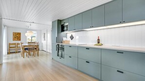 Uma cozinha moderna com armários azul-claros, bancada branca e um espaço de refeições com cadeiras e mesa de madeira.
