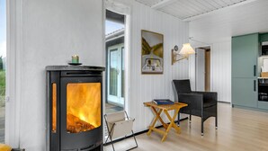 Um quarto acolhedor com uma lareira a lenha, uma cadeira de vime, uma mesa pequena e um quadro na parede.