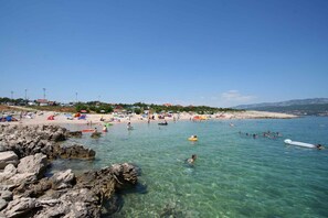 Una playa con agua cristalina, costa rocosa y gente nadando y tomando el sol.