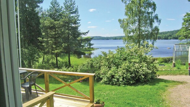 A wooden deck with a railing, potted plants, and a view of a lake surrounded by trees.