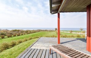 Une terrasse en bois avec un banc, offrant une vue sur un paysage verdoyant et la mer.