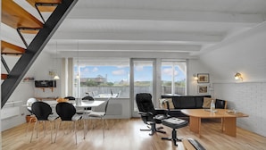 A modern loft-style living space with a dining area, a black leather sofa, and a wooden dining table. - Beach front home in Hvide Sande with WiFi (Hvide Sande)