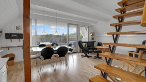 A modern interior with a dining area, wooden staircase, and large windows offering a view. - Beach front home in Hvide Sande with WiFi (Hvide Sande)
