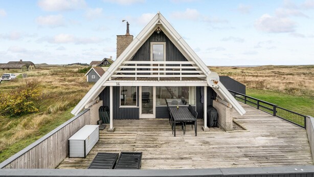 A modern house with a triangular roof, a covered patio with outdoor furniture, and a view of the surrounding landscape. - Beach front home in Hvide Sande with WiFi (Hvide Sande)