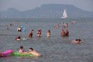 Ein voller Strand mit badenden Menschen und Wassersportlern auf verschiedenen Wasserfahrzeugen.