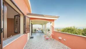 A covered outdoor area with a table and chairs, a view of the sea, and a building with wooden doors and a tiled floor. - 2 bedroom awesome home in Badesi OT (Badesi OT)