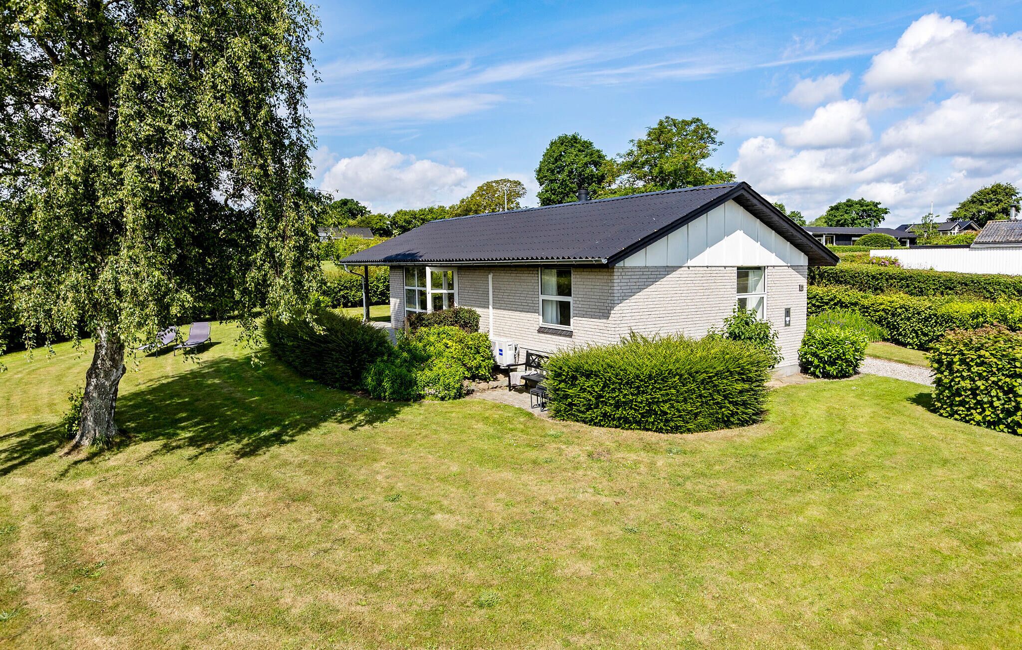 Een gelijkvloers huis met een donker dak, omgeven door verzorgd gras en hagen.