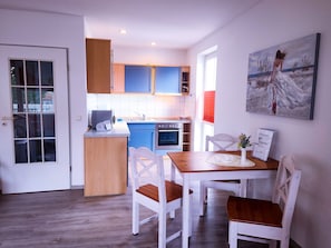 Une cuisine moderne avec des meubles bleus, un plan de travail en bois et un coin repas avec des chaises et une table blanches.