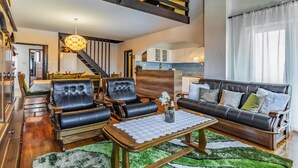 Een ruime woonkamer met leren banken, een houten salontafel en een trap naar een verdieping erboven.