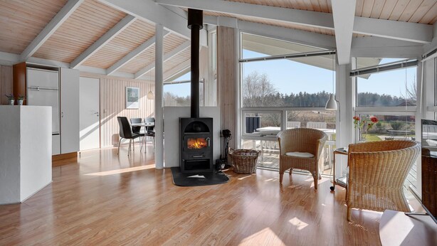 A spacious room with a large wooden ceiling, a black wood stove, wicker furniture, and large windows offering a view of the outdoors.