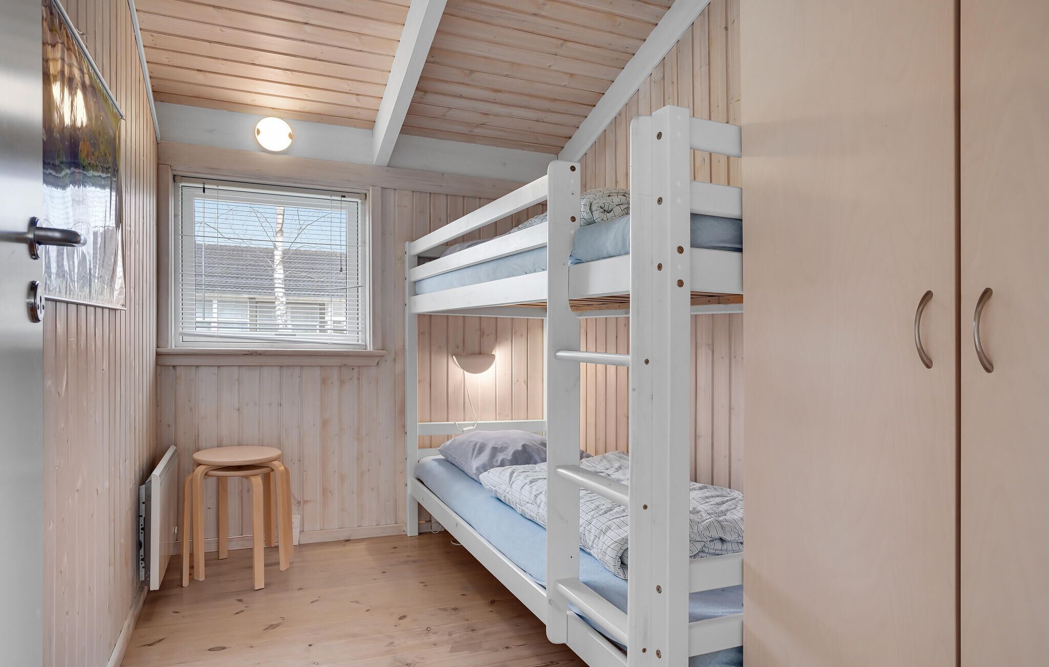 Une petite pièce avec un lit superposé, une petite table et une fenêtre avec des stores.