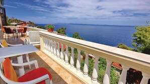 Un balcone con vista sul mare, arredi da esterno e una ringhiera.