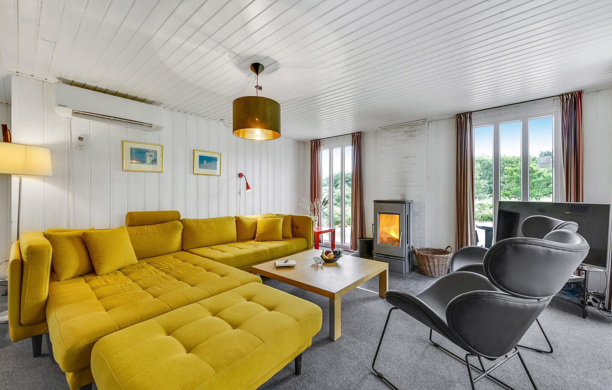 En moderne stue med en gul sofa, et træbord, en pejs og et fjernsyn.