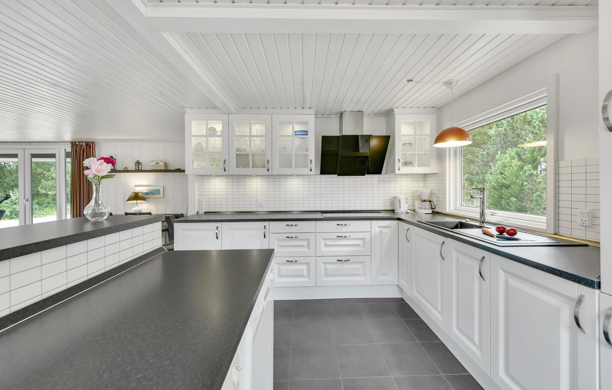 Eine moderne Küche mit weißen Schränken, einem großen Fenster und Blick ins Grüne.