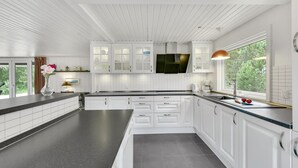 Ett modernt kök med vita skåp, ett stort fönster och utsikt över grönområden utanför.