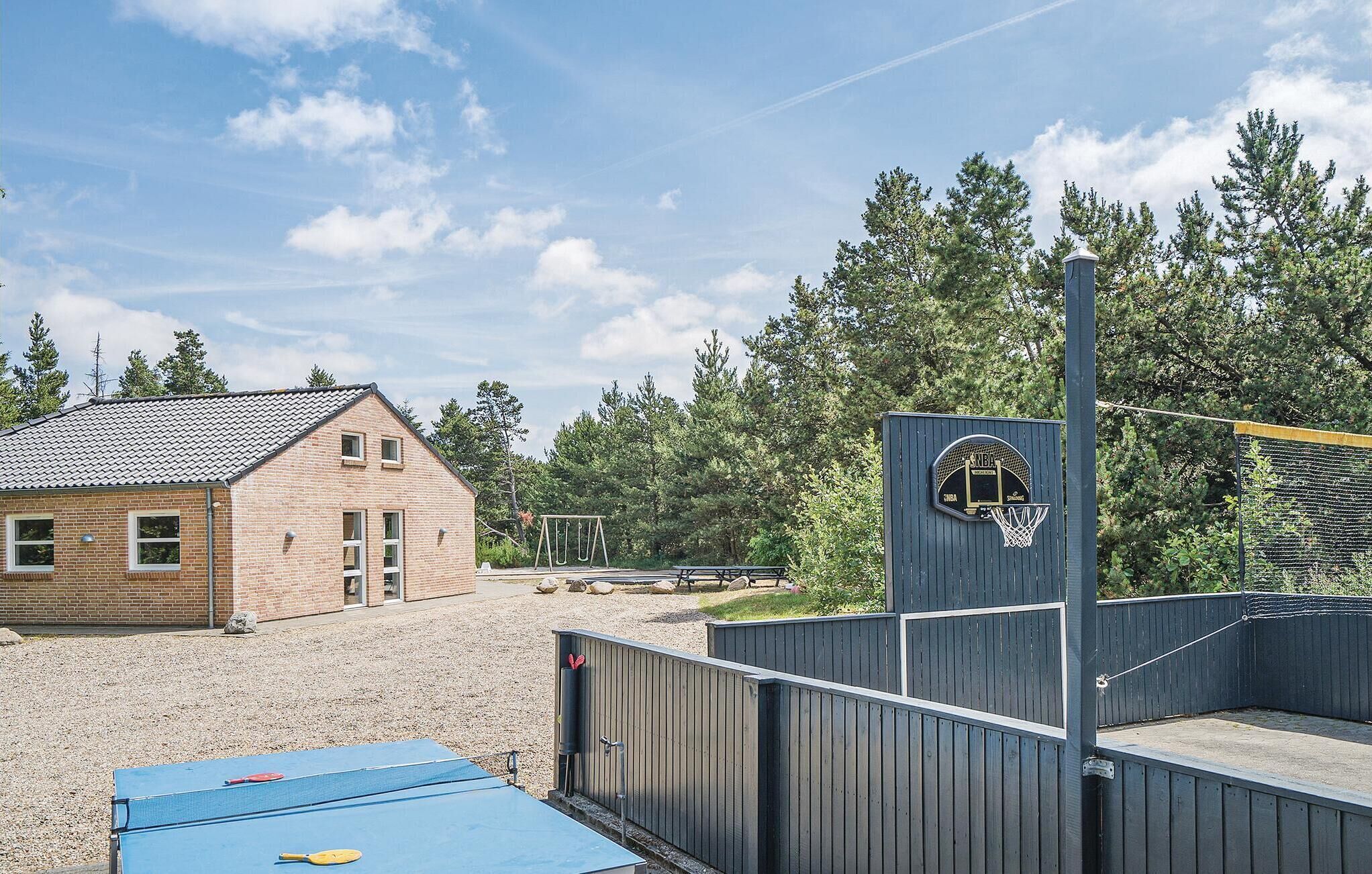 A basketball court with a net, a wooden fence, and a building in the background.