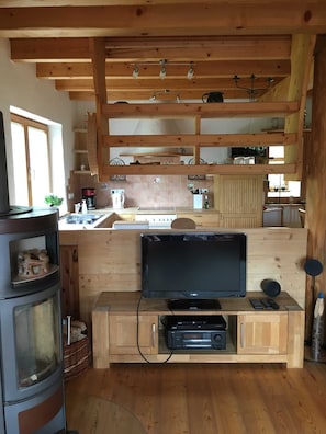 Una cocina compacta con vigas de madera, televisor integrado y estufa de leña.