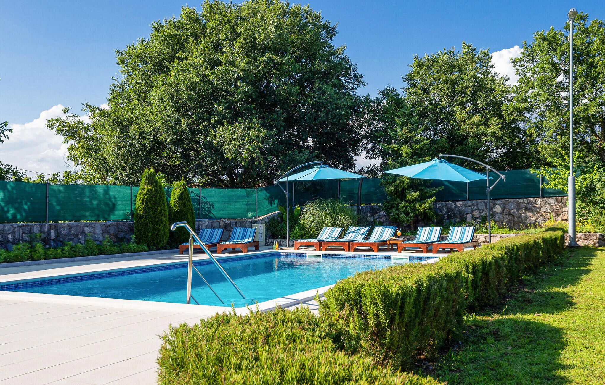 Une piscine entourée de verdure et de murs de pierre, avec des chaises longues et des parasols.
