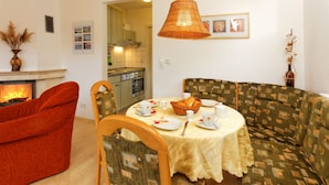 Una sala de estar acogedora con chimenea, una mesa de comedor con platos y tazas, un sofá estampado y una cocina al fondo.