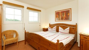 Un dormitorio con una cama de madera, dos mesitas de noche, una silla de mimbre y un cuadro en la pared.