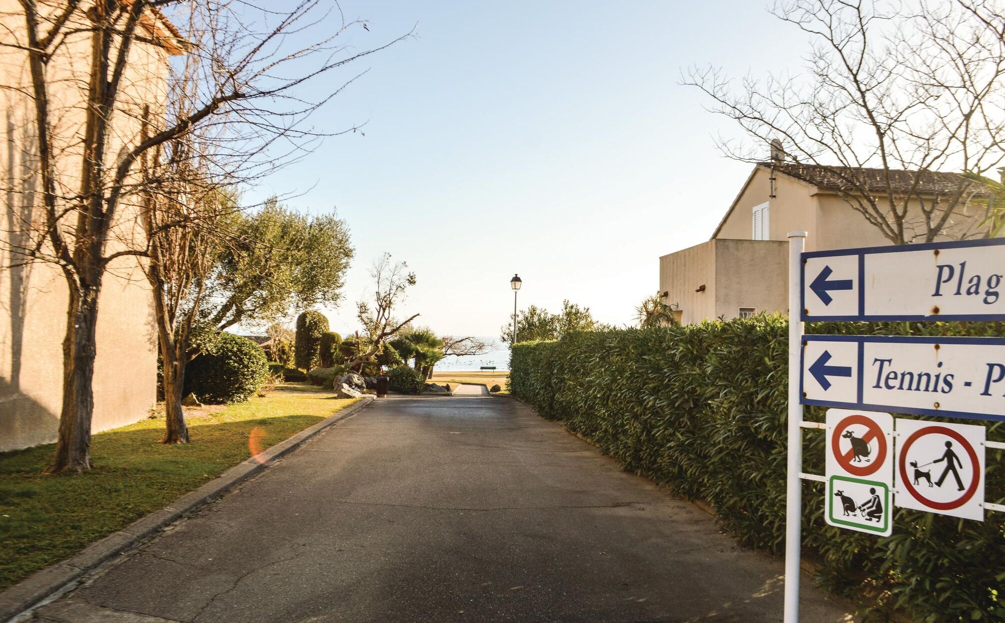 A pathway leading to a beach with directional signs for 'Plag' and 'Tennis - P'.