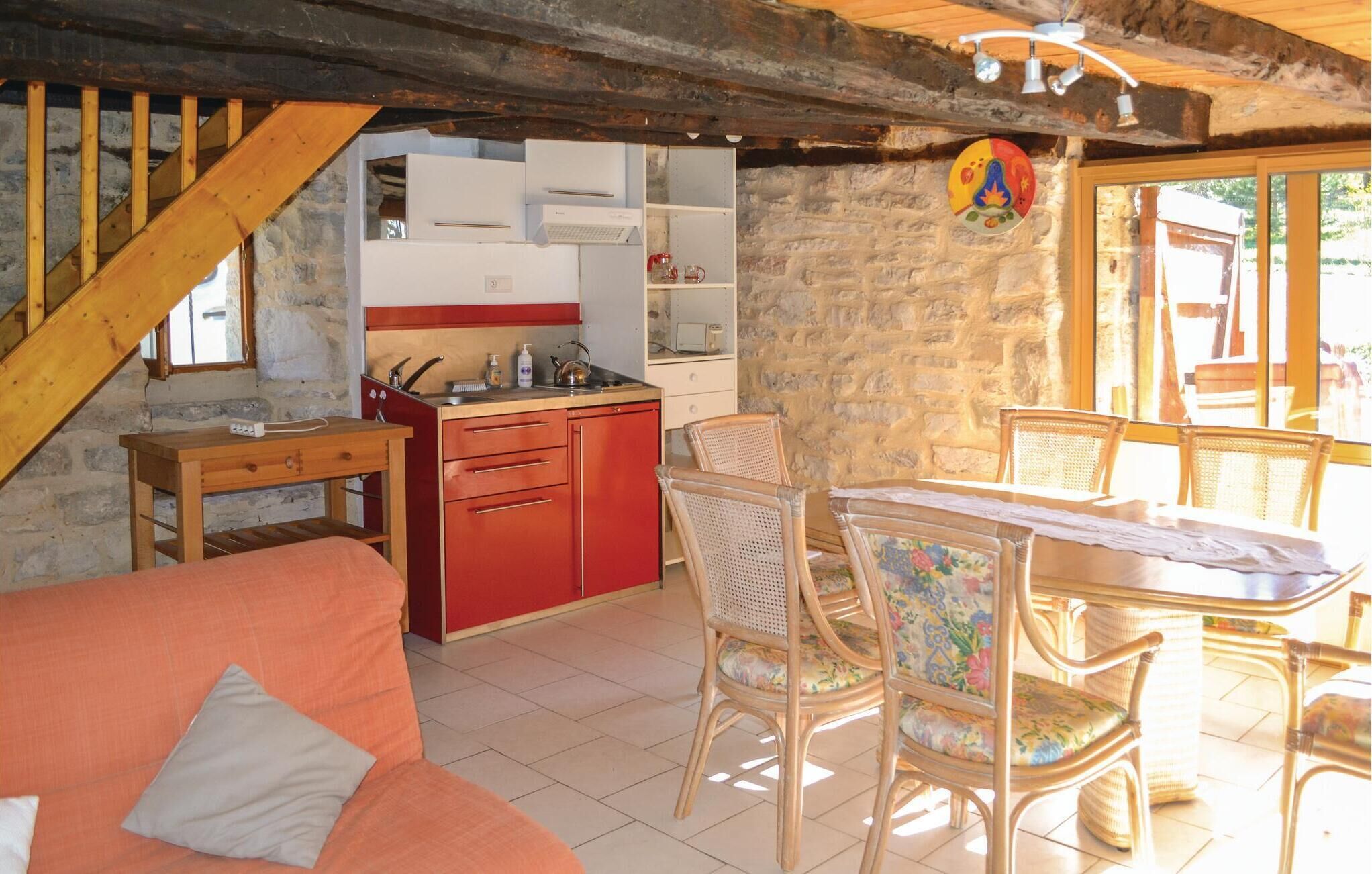 A cozy room with a wooden staircase, a kitchenette with red cabinets, wicker chairs, and a dining table.