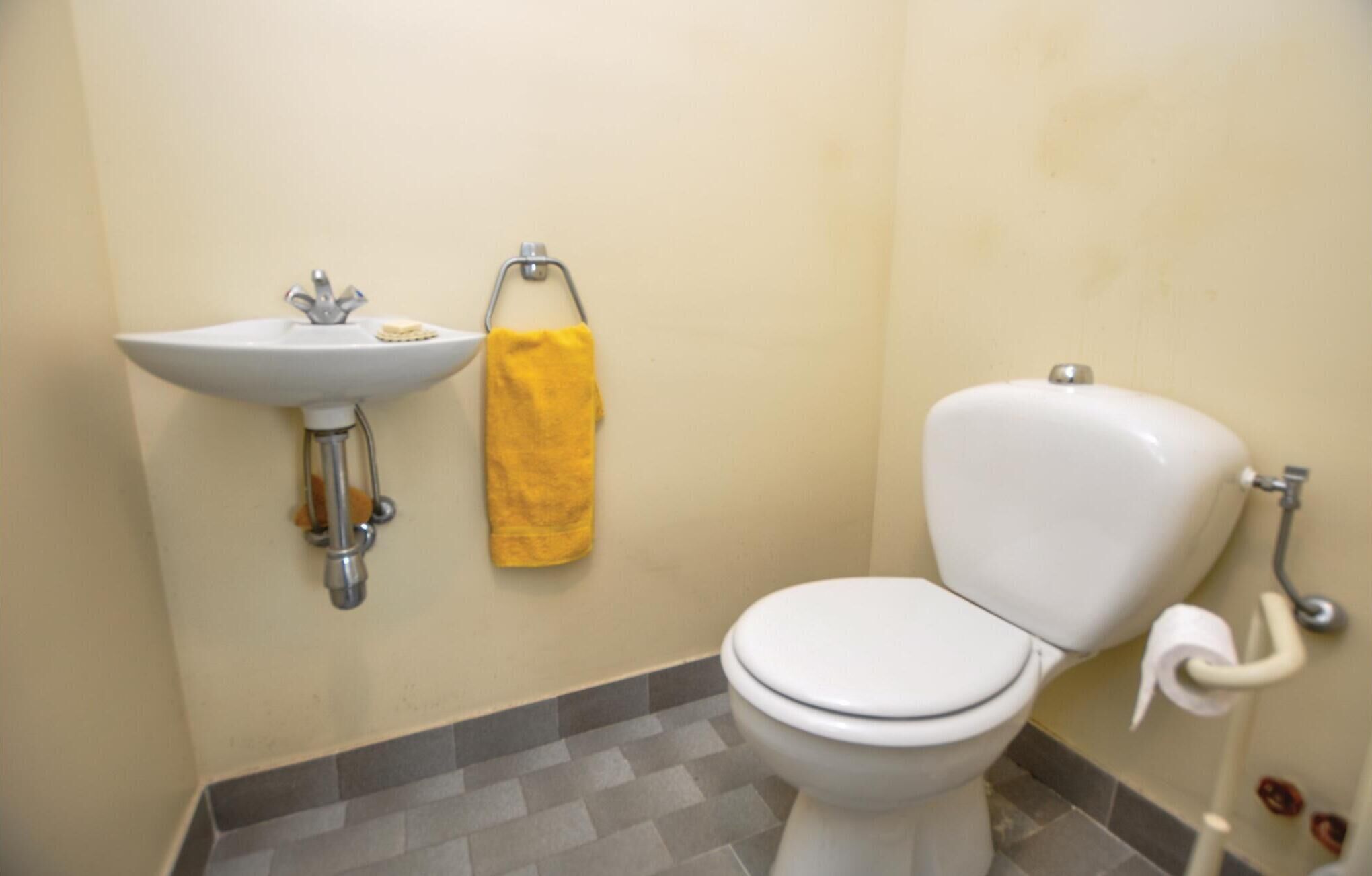 Une salle de bain avec un lavabo blanc, une serviette jaune et des toilettes.