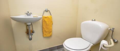 Une salle de bain avec un lavabo blanc, une serviette jaune et des toilettes.