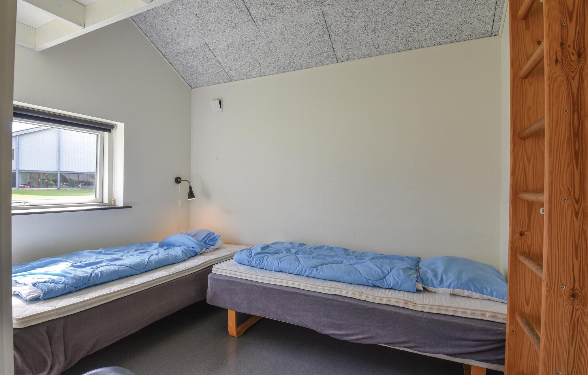 A small, single-room accommodation with two single beds, a window, and a ceiling light.