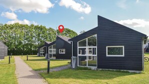 A row of modern, dark-colored cabins with large windows, a paved path leading to them, and a red location marker in the sky.