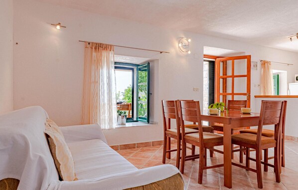 Une pièce confortable avec un canapé, une table à manger et des chaises, une fenêtre avec des rideaux et une vue sur la verdure à l’extérieur.