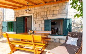 Un bâtiment en pierre avec des poutres et des volets en bois, une table et des bancs en bois, et un canapé avec un coussin.