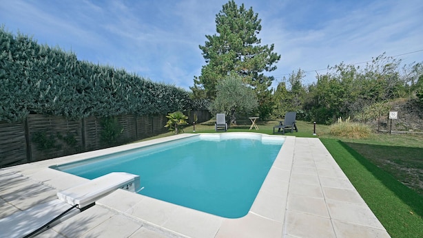 A rectangular swimming pool with a tiled deck, two lounge chairs, and a tall evergreen tree in the background. - 3 bedroom nice home in Mazan (Mazan)
