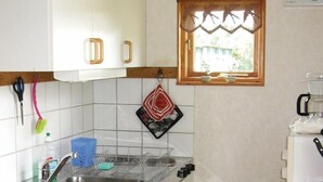 Cozinha compacta com armários brancos, pia de aço inoxidável e uma pequena janela com moldura de madeira.