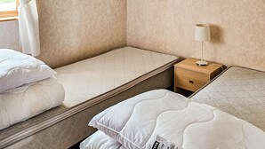 Quarto de hotel com duas camas de solteiro, mesa de cabeceira com abajur e janela com cortinas.