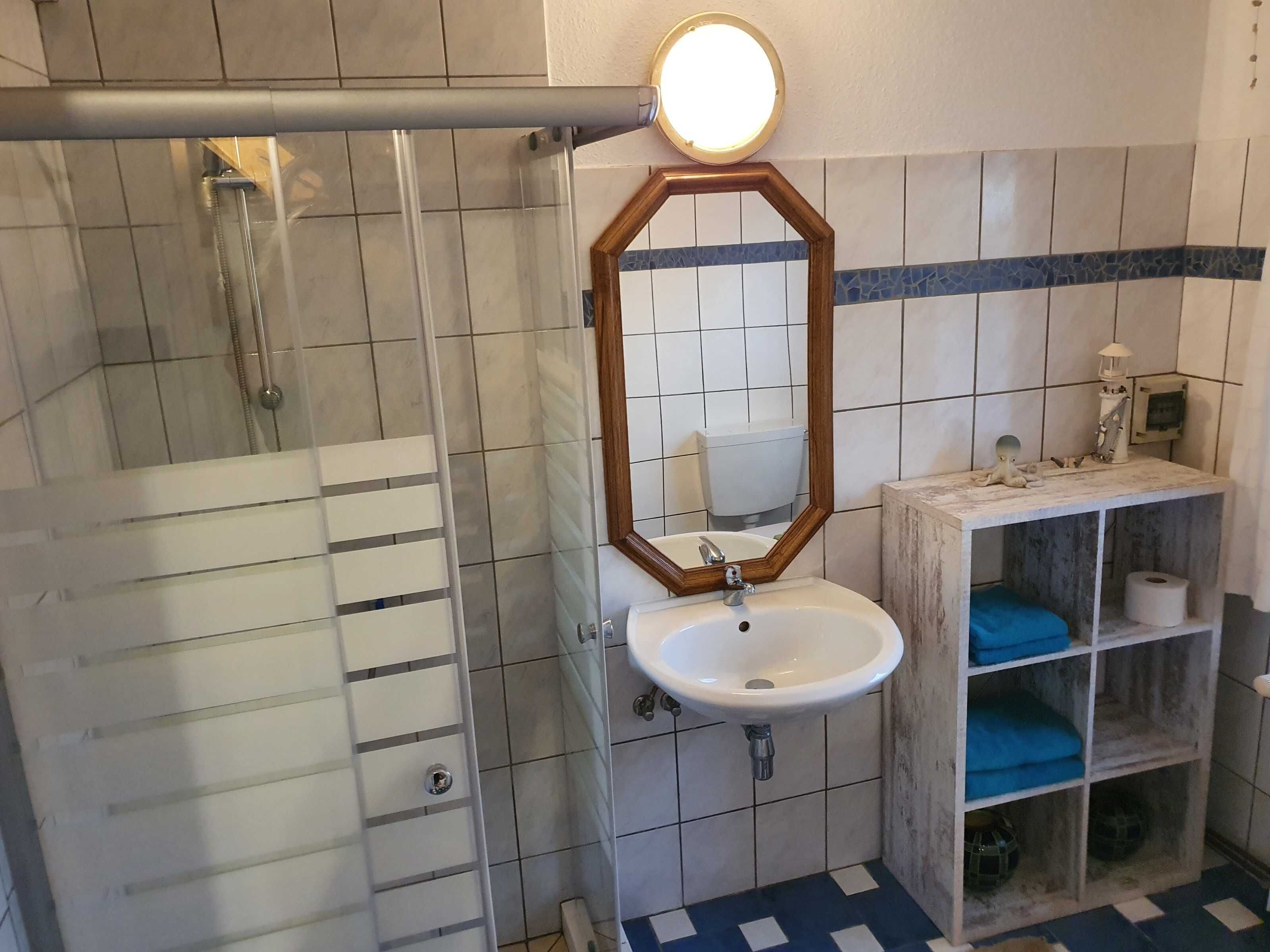 Ein Badezimmer mit Dusche, Waschbecken, Spiegel und einem Ablagefach mit Handtüchern.