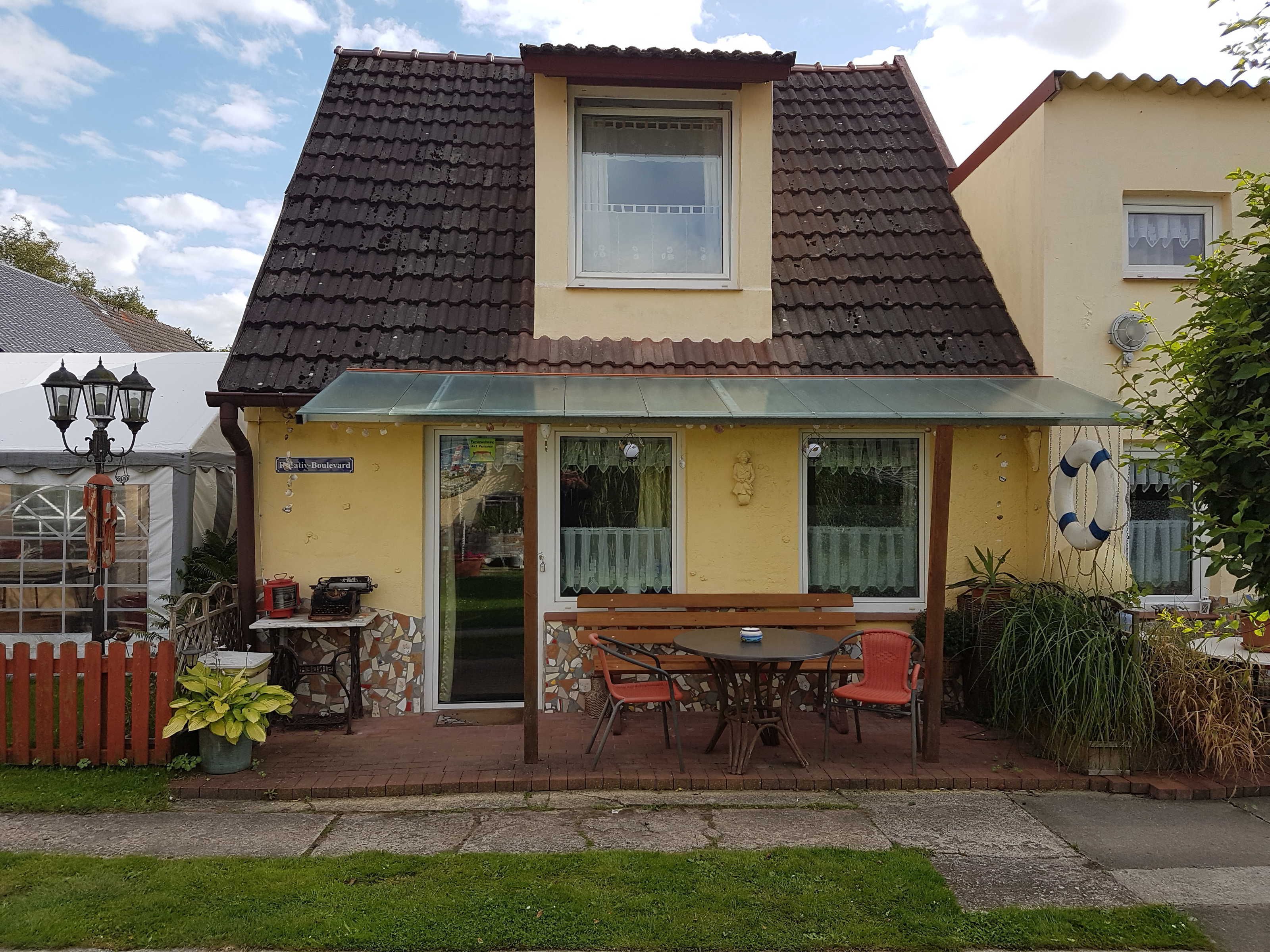 Una casa con tetto in tegole, un portico coperto con tavolo e sedie, e un piccolo giardino.