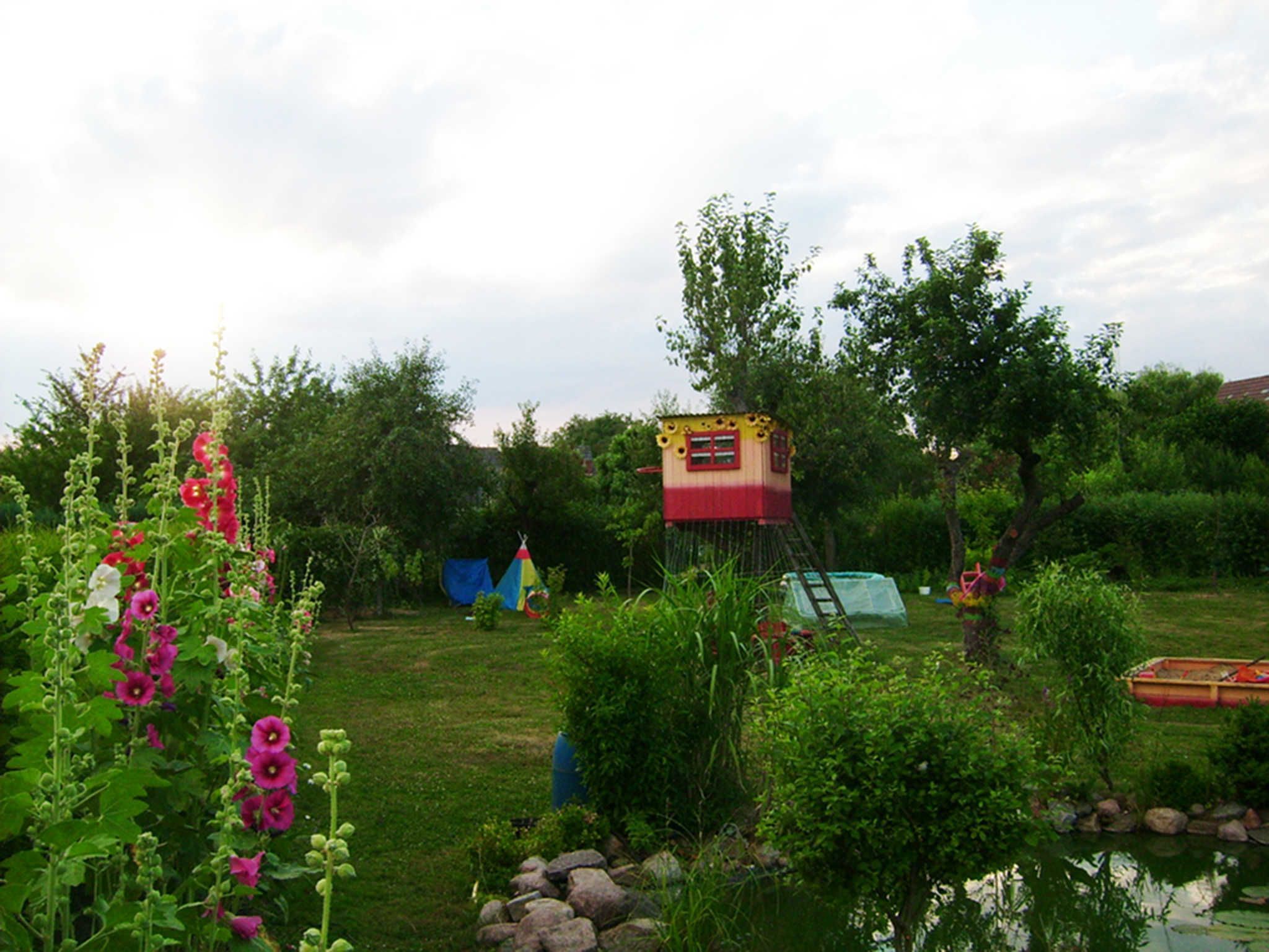A garden with a small treehouse, a tent, and a pond.