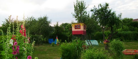 A garden with a small treehouse, a tent, and a pond.