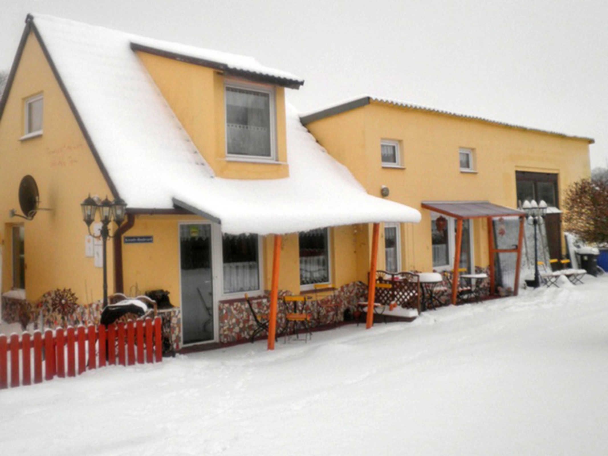 Un bâtiment jaune avec un toit enneigé, un patio couvert et une clôture rouge.