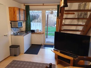 Ein kompakter Wohnraum mit Küchenzeile, Fernseher und Blick durch eine Glastür.