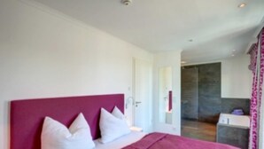 A modern bedroom with a large bed, white pillows, and a pink headboard. - Villa Lara Whg.11, LAKE VIEW, ROOF TERRACE, CHAIR - Villa Lara, NEAR THE BEACH, (Heringsdorf)