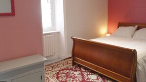 A bedroom with a wooden bed, a radiator, a window, and a patterned carpet. - Gorgeous apartment in Vildé-la-Marine (Vildé-la-Marine)