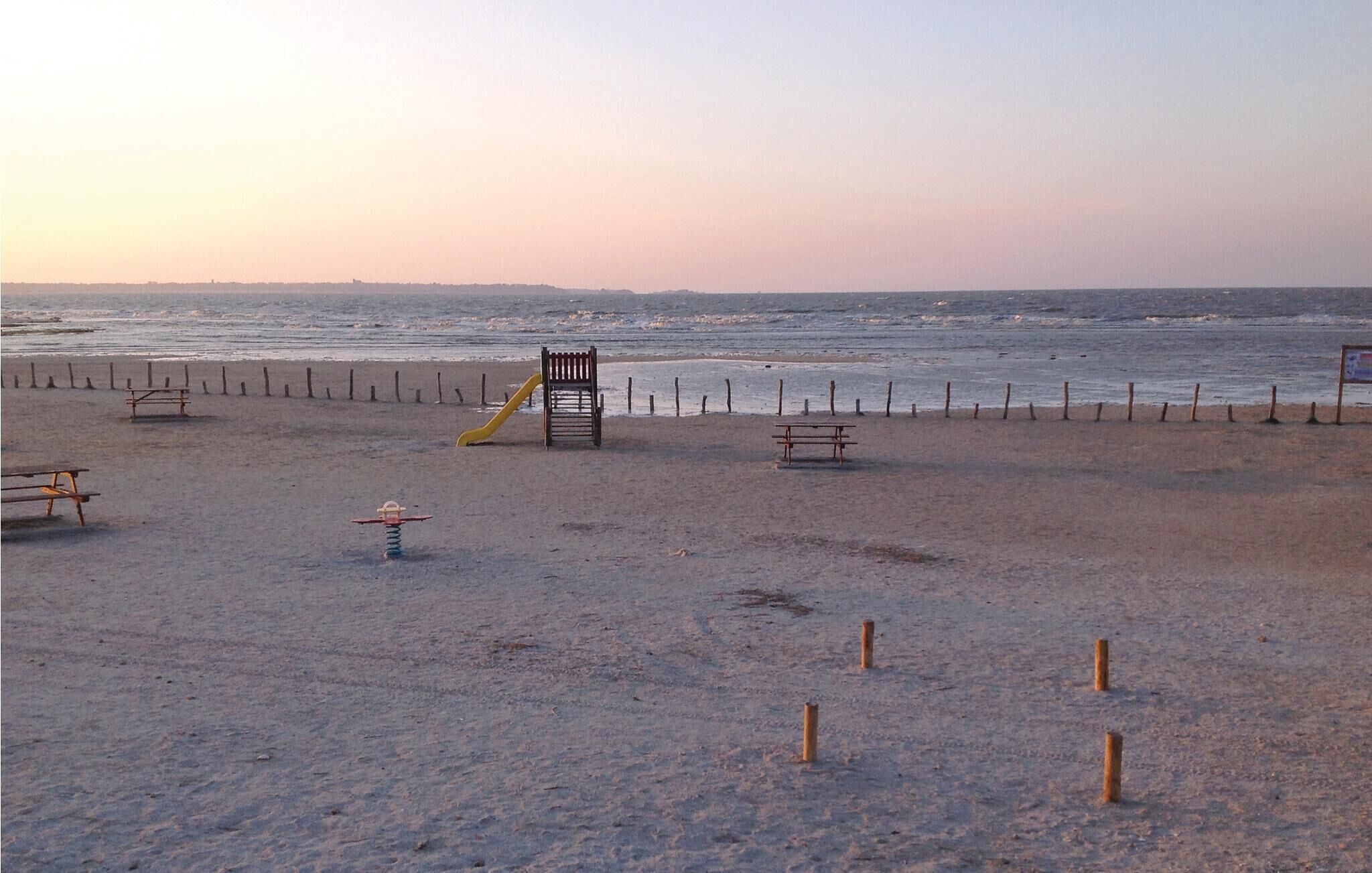 Une plage avec une aire de jeux, comprenant un toboggan et des balançoires, ainsi que plusieurs bancs.