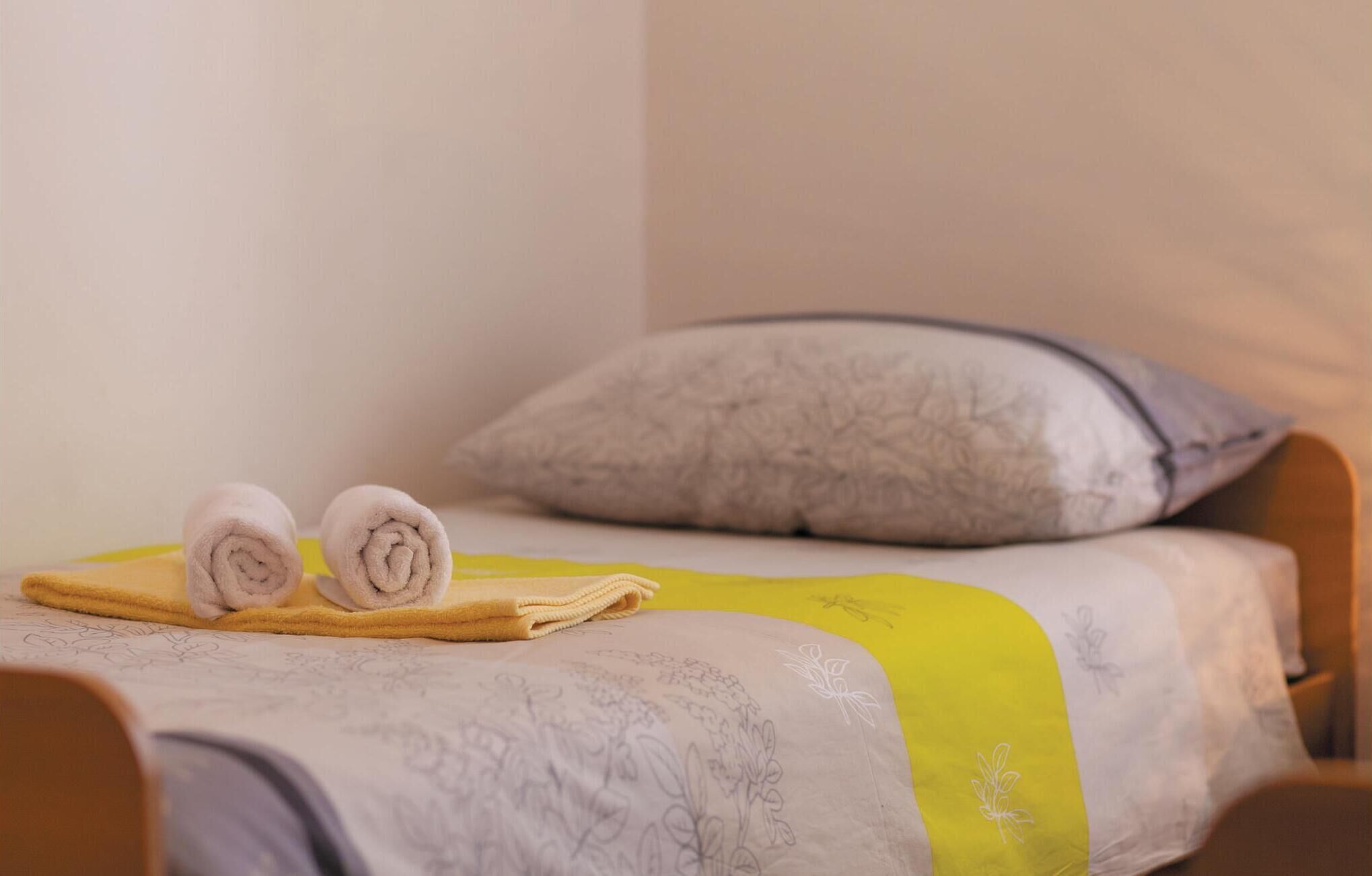 A neatly made bed with rolled towels, a floral-patterned bedspread, and a pillow with a gray and white design.
