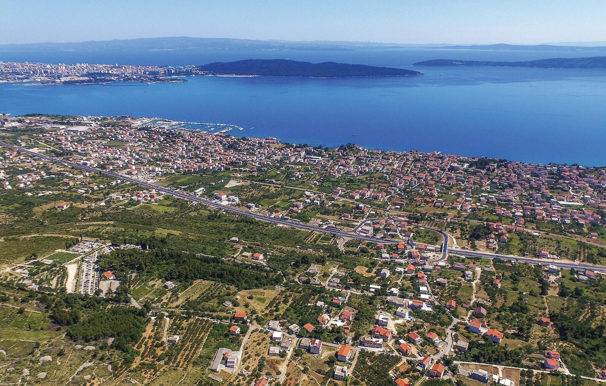 Vue aérienne d’une ville côtière, avec un ensemble dense de maisons aux toits rouges, une route principale et un port de plaisance.